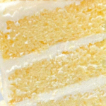 Champagne Velvet Cake with pink champagne frosting, sliced and topped with edible pearls, on a white cake stand.